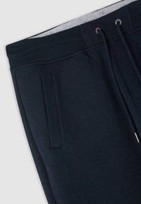 Ciemnoniebieskie dresy z żeberkowym pasem, kieszenią boczną oraz sznurkiem z metalowymi oczkami i końcówkami, zaprezentowane na jasnym tle.