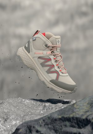 Hellgrauer und korallenfarbener Wanderschuh, der über felsigem Gelände schwebt, mit strukturierter Sohle und verstärktem Knöchelschutz.