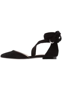 Scarpa piatta in suede nera con punta appuntita e cinghie incrociate alla caviglia con fibbia argentata, vista di lato su sfondo bianco.