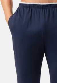 Marineblauwe sportbroek met een zachte textuur, elastische tailleband en zijzakken. Soepele stof en eenvoudig ontwerp.