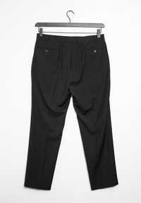 Svarta skräddarsydda byxor hängande utställda. Funktioner inkluderar två bakfickor med knäppningar och en slät textur.