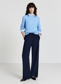 Pull en tricot bleu clair à manches longues et col côtelé, associé à un pantalon large taille haute bleu marine et des chaussures à bout pointu noires.