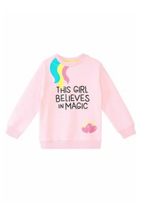 Rosa sweatshirt med stor svart text, "DEN HÄR FLICKAN TROR PÅ MAGI," med färgglada regnbågsdetaljer och hjärt-grafik i nederdelen.