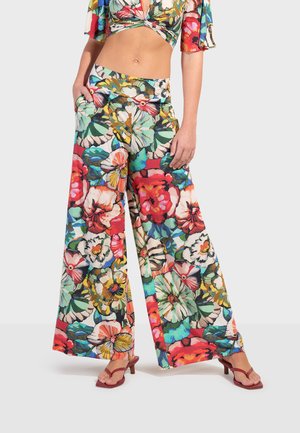 Vrouw draagt wijde broekspijpen en een bijpassende cropped blouse met een kleurrijke, grote bloemenprint, gecombineerd met rode sandalen met hak.