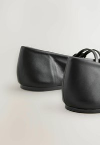 Mustat nahkakengät litteällä pohjalla, pyöristetyn nenän, sileällä pinnalla ja minimalistisella muotoilulla. Pohjat ovat täysin litteät, mutta takana on hieman kantapää.