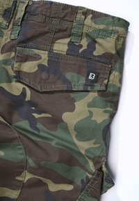 Tasca posteriore di pantaloni cargo mimetici verdi e marroni con patta e piccola etichetta nera del marchio su sfondo bianco.