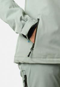 Light green jacket with a zippered pocket. Features elastic cuffs and a tag near the zipper. Soft texture and streamlined design.