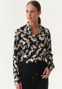 Collared blouse in black with a floral leaf pattern in light blue and beige. Long sleeves, button closure, smooth fabric texture.
