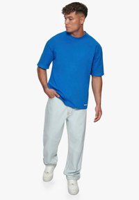 Blå bomulds t-shirt med korte ærmer, ribbet rund hals, kombineret med lyse denimjeans og hvide sneakers. Har et synligt logo-tag.