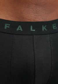 Schwarze Boxer-Briefs mit einer weichen Textur, einem grünen Markenbund und einem sicheren Sitz mit Nahtdetails.