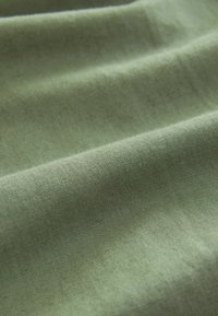 Puha, texturált zöld szövet, látható ráncokkal és redőkkel, könnyű anyagból készült, sima felülettel és finom fénylő felülettel.