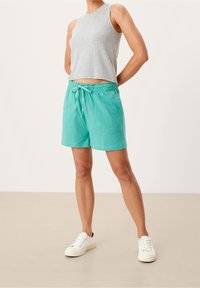 Szary bezrękawnik zestawiony z turkusowymi szortami z elastycznym pasem i sznurkiem. Całość dopełniają białe trampki.