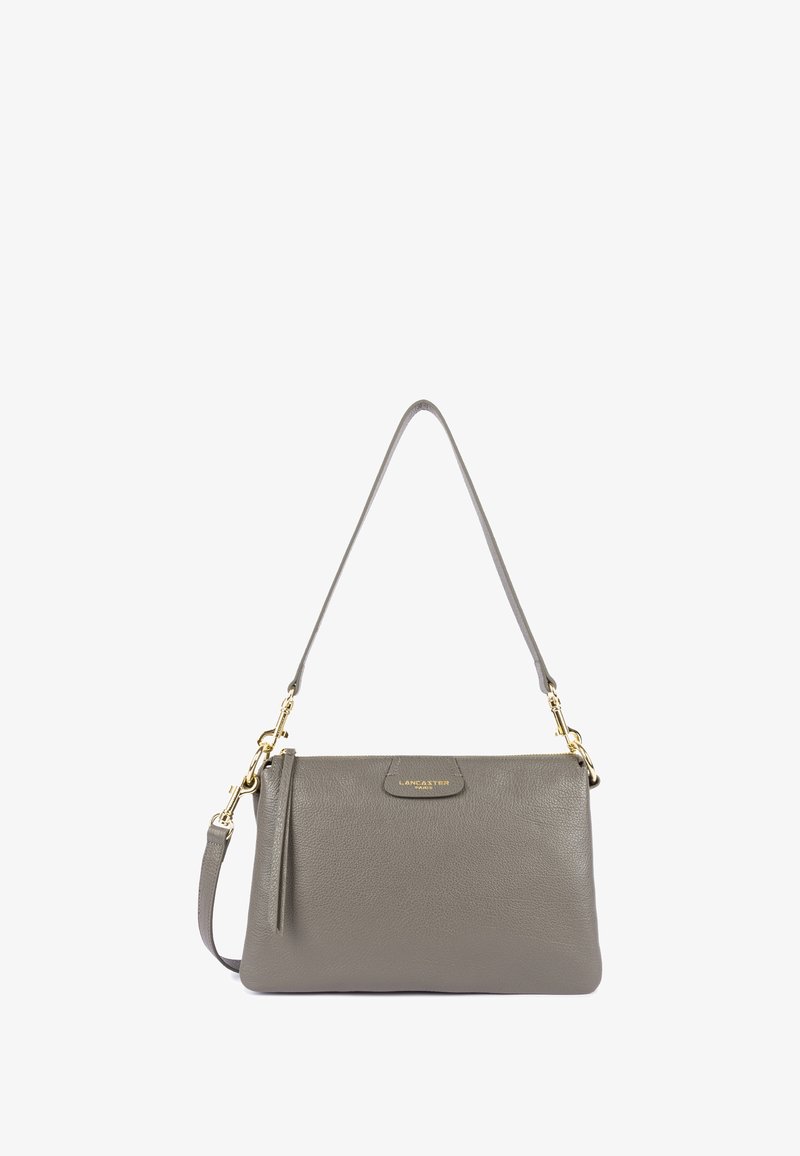 Sac à main en cuir gris avec une texture lisse, doté d'une bandoulière amovible et de détails en or. Il a une forme arrondie avec un accent de logo.