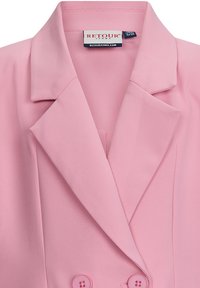 Bladoróżowy żakiet wykonany z miękkiej tkaniny, z wyciętym kołnierzem, podwójnym zapięciem na guziki i bocznymi kieszeniami.