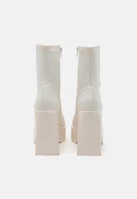 White synthetic ankle boots with a smooth texture, chunky beige platform heels, and a zip closure on the back.