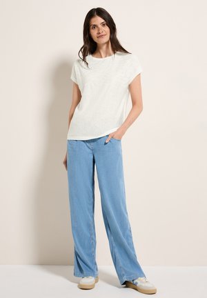 Haut blanc à manches courtes avec une texture subtile, associé à un jean large bleu clair. Des baskets claires avec des accents beige complètent le look.