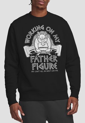 Black sweatshirt featuring a humorous graphic of a muscular character lifting weights, with the text "WORKING ON MY FATHER FIGURE" prominently displayed.