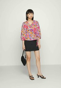 Top envolvente floral com flores laranja e cor-de-rosa, mangas longas e um detalhe de laço. Combinado com uma saia mini preta e sandálias pretas com tiras.