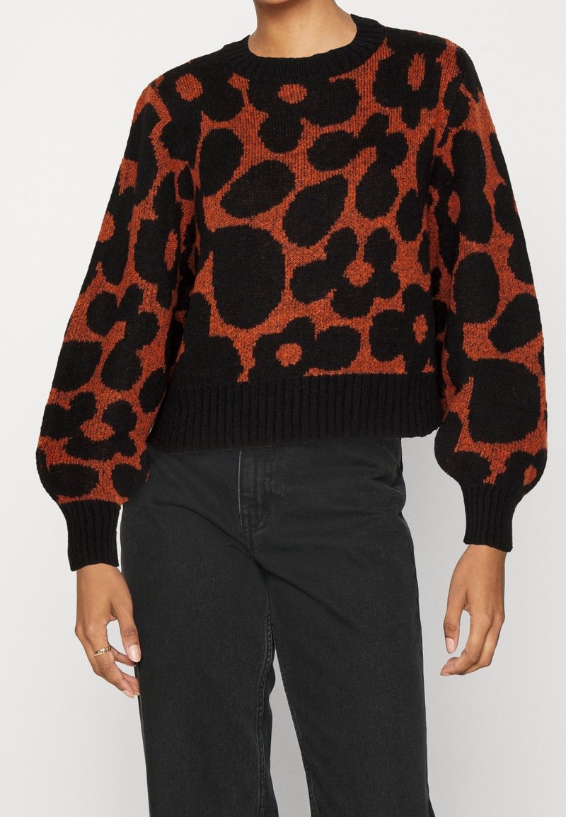 Pull imprimé léopard noir et orange brûlé avec manches ballon porté avec un jean noir taille haute, raccourci à la taille.