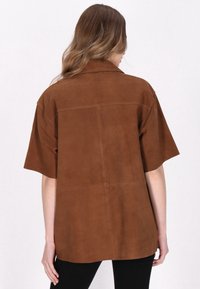 Hnědá sukně z nubuku s krátkými rukávy, volný střih, viditelné švy a design zadního yoku. Rovný lem, minimalistický styl.