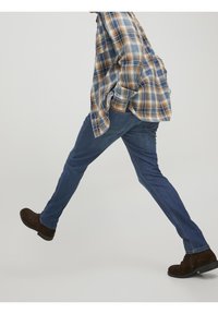 Blå denimjeans med rak passform, med en subtil tvätt, i kombination med en rutig skjorta i bruna, blå och beige nyanser, samt bruna stövlar.