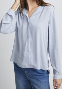 Blusa azzurro chiaro con colletto, maniche lunghe e vestibilità comoda. Realizzata in tessuto morbido con chiusura a bottoni e spacchi laterali per facilitare i movimenti.