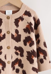 Cardigan beige avec un motif léopard en brun foncé et orange rouille. Encolure côtelée et fermeture à boutons avec des boutons de marque.