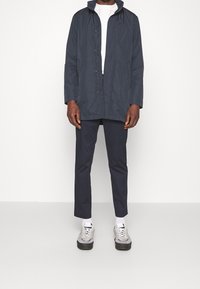 Marinblå vattentålig jacka med dragkedja, justerbar krage och sidofickor, i kombination med marinblå byxor och grå sneakers.