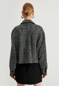 Zwart-wit geruite blazer met een cropped ontwerp, oversized silhouet en knoopmanchetten, gedragen over een gestructureerde zwarte rok.