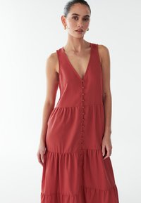 Pruunika vase toonis maksikleidi sügava V-kaelusega, varrukateta ja nööpidega esiküljel. Omadusena on kihilised volangid ja pehme, tekstuuriga kangas.