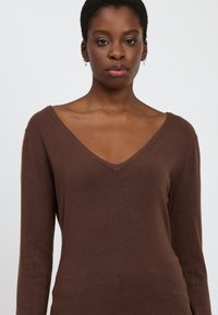 Brauner Strickpullover mit langen Ärmeln, V-Ausschnitt und weichem Material. Die taillierte Passform betont die Silhouette und eignet sich gut zum Schichten.