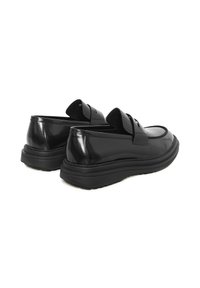 Mocasines de charol negro con una gruesa suela de goma negra, que cuentan con un diseño sin cordones y detalles de doble tira en la parte delantera.
