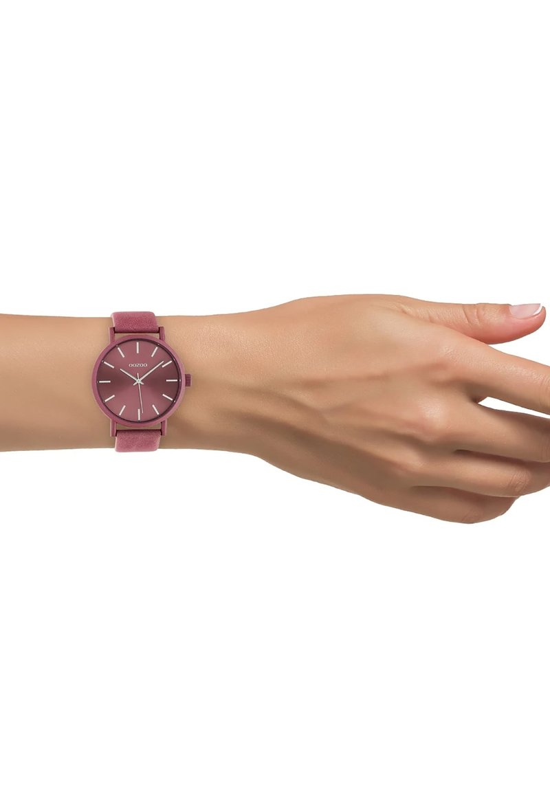 Round watch with a burgundy face and matching fabric strap. Silver hour markers and hands. Minimalist design on a wrist.