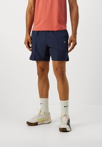 Navy athletic shorts with side pockets, paired with a peach shirt, white Nike socks, and light sneakers featuring a yellow accent.
