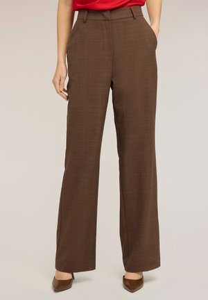 Personne portant un pantalon à jambes larges à taille haute en tartan marron avec des poches avant, assorti à des chaussures marron pointues et un haut rouge.