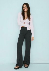 Svijetloružičasti rebrasti kardigan s gumbima, uparen s tamnim hlačama širokih nogavica visokog struka i crnim ravnim sandalama. Minimalistički dizajn.