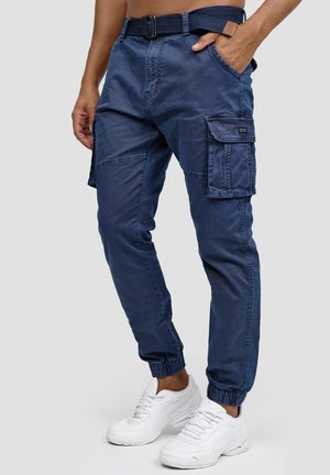 Pantalones cargo azul marino con cintura con cinturón, puños elásticos, múltiples bolsillos y una textura suave, combinados con zapatillas blancas.