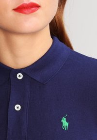 Námořnická modrá polo tričko s texturovanou tkaninou, s zeleným vyšitým logem, dvěma bílými knoflíky a klasickým designem límce.