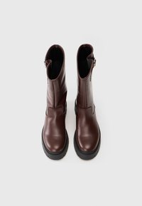 Botas de tobillo de cuero marrón con un acabado suave, punta redondeada y suela gruesa negra. Presentan una cremallera lateral y un ligero tacón.