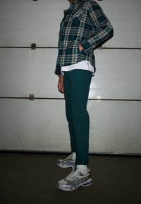 Károvaná flanelová košile v odstínech teal a béžové, spojená s teal tepláky. Stříbrné sportovní boty s modrými akcenty dokončují celý outfit.