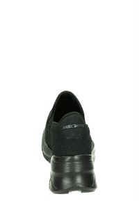 Svarta Skechers-skor sedda från baksidan, med en mesh-övre och dämpad sula, som framhäver deras lätta design och komfort.