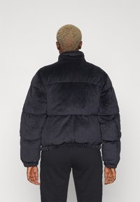 Giacca puffer blu navy con colletto alto, realizzata in materiale morbidissimo, presenta una vita arricciata e polsini elasticizzati. Tessuto liscio.