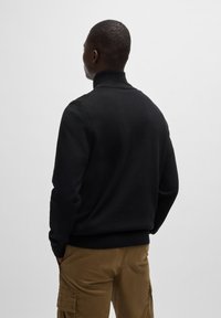 Zwarte gebreide trui met een hoge kraag en lange mouwen, met een slim fit ontwerp. Zachte textuur, eenvoudig en minimalistisch stijl.