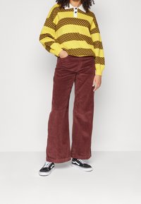Yellow and brown striped sweater with a white collar, paired with maroon corduroy wide-leg pants and black sneakers.