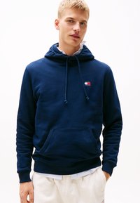Navy blauwe hoodie van katoen met een voorkantzak, verstelbare trekkoordcapuchon en klein logo met rood, wit en blauwe accenten.