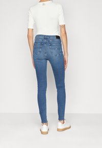 Välpassande, mörkblå denimjeans med en slät textur, medelhög midja och bruna accenter på vita sneakers. Bakifrån visas fickdesignen.