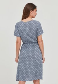Modrá vzorovaná šaty s krátkymi rukávmi, výstrihom do V, elastickým pásom, sukňou dĺžky po kolená a geometrickým dizajnom.