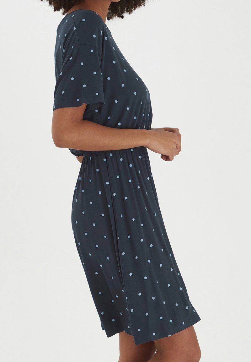 Robe à manches courtes bleu marine ornée de pois bleu clair. Le tissu est doux avec une coupe décontractée et une taille élastique, créant une silhouette fluide.