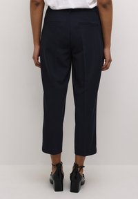 Pantalons navy sur mesure avec un design raccourci, dotés d'une texture lisse, de passants de ceinture, de deux poches arrière et d'une coupe droite.