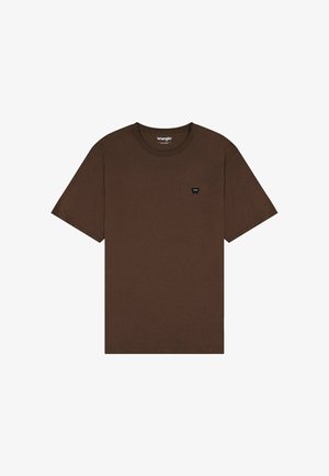 Camiseta de algodón marrón con mangas cortas, escote redondo y un pequeño parche de logo negro en el lado izquierdo del pecho. Diseño simple, sin patrones.